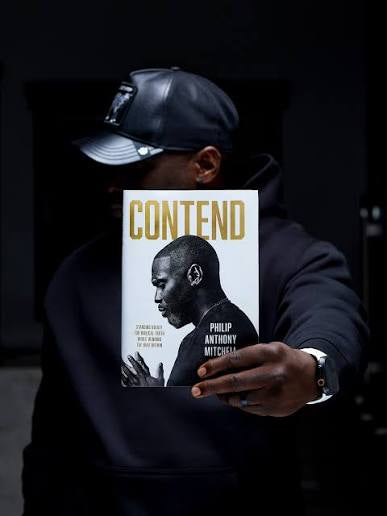 Hardcover copy of Contend by Philip Anthony Mitchell held up to the camera against a dark background
