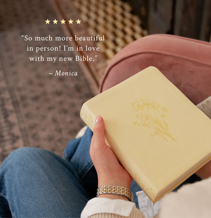 A person holds a pale yellow Bible with a gold floral embossing on the cover, seated on a pink armchair with blue jeans visible. A quote from Monica appears on the left against a warm indoor background.